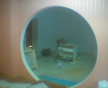 Nietypowe okrągłe przejście w ścianie, widok na wnętrze w trakcie remontu, widoczne meble i narzędzia, surowe wykończenie.